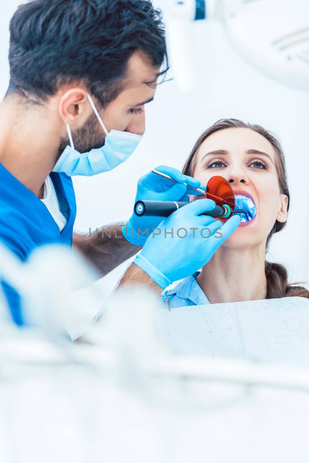 Young woman during innovative oral treatment with cordless LED curing light machine for whitening and restoration in the dental office of an experienced dentist