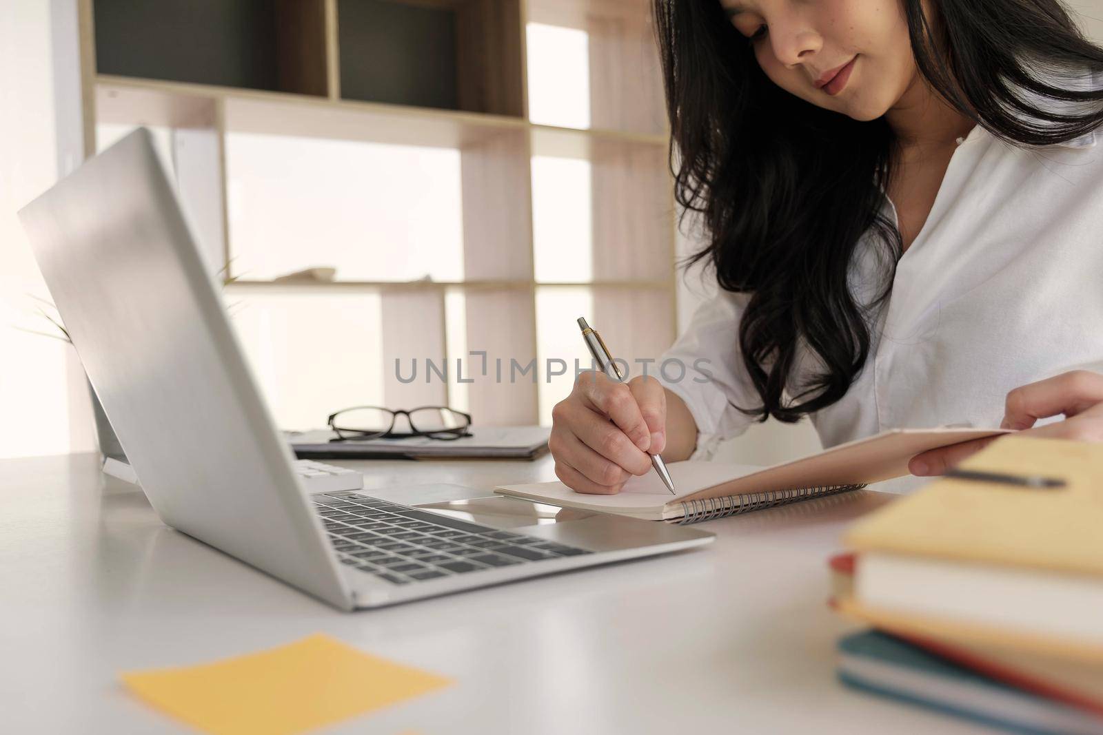 Young business woman taking notes in notebook.On table is laptop for online learning or business finance concept by nateemee