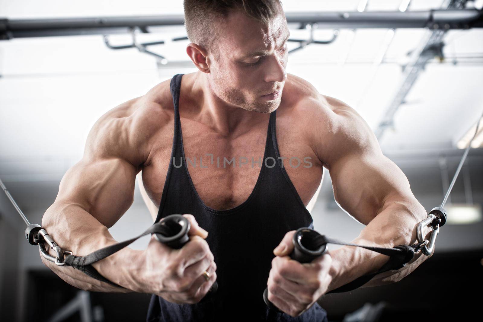 Bodybuilder doing butterfly on cable pull for better definition of his arm muscles