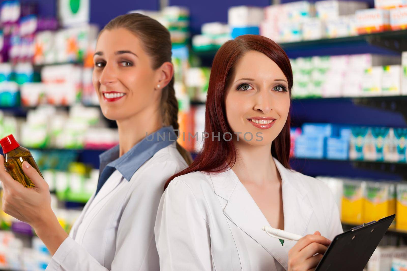 Pharmacist with female assistant in pharmacy standing in front of shelf with drugs