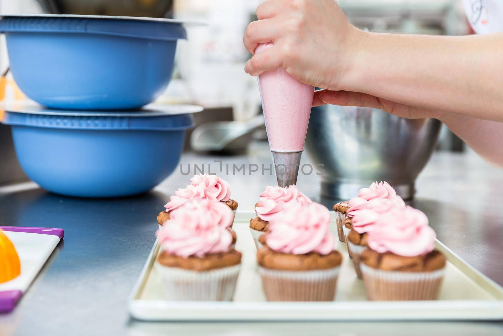 Women in pastry bakery as confectioner glazing muffins with icing bag, close-up