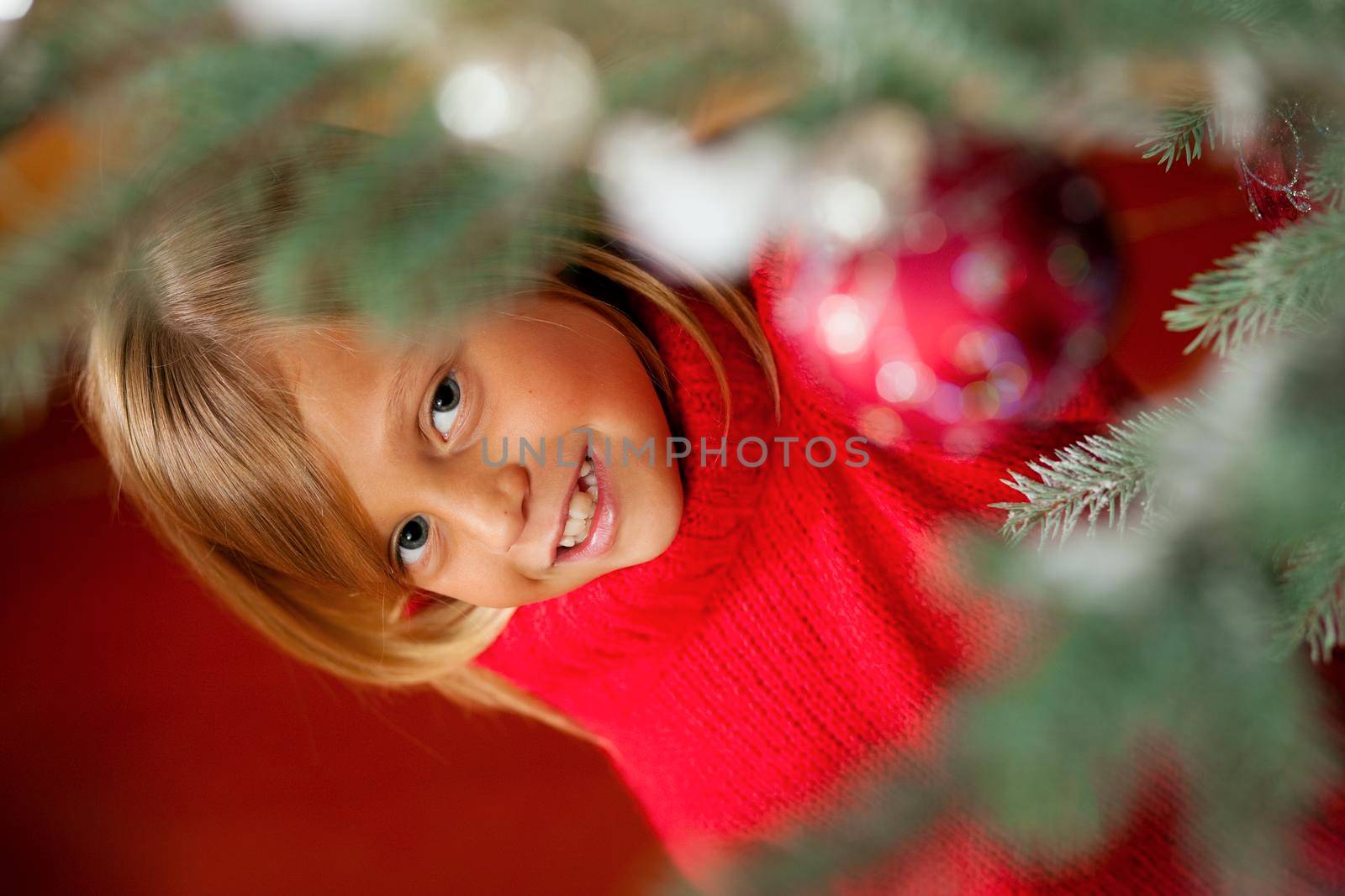 Young girl helping decorating the Christmas tree, holding some Christmas baubles in her hand (Focus on girl)