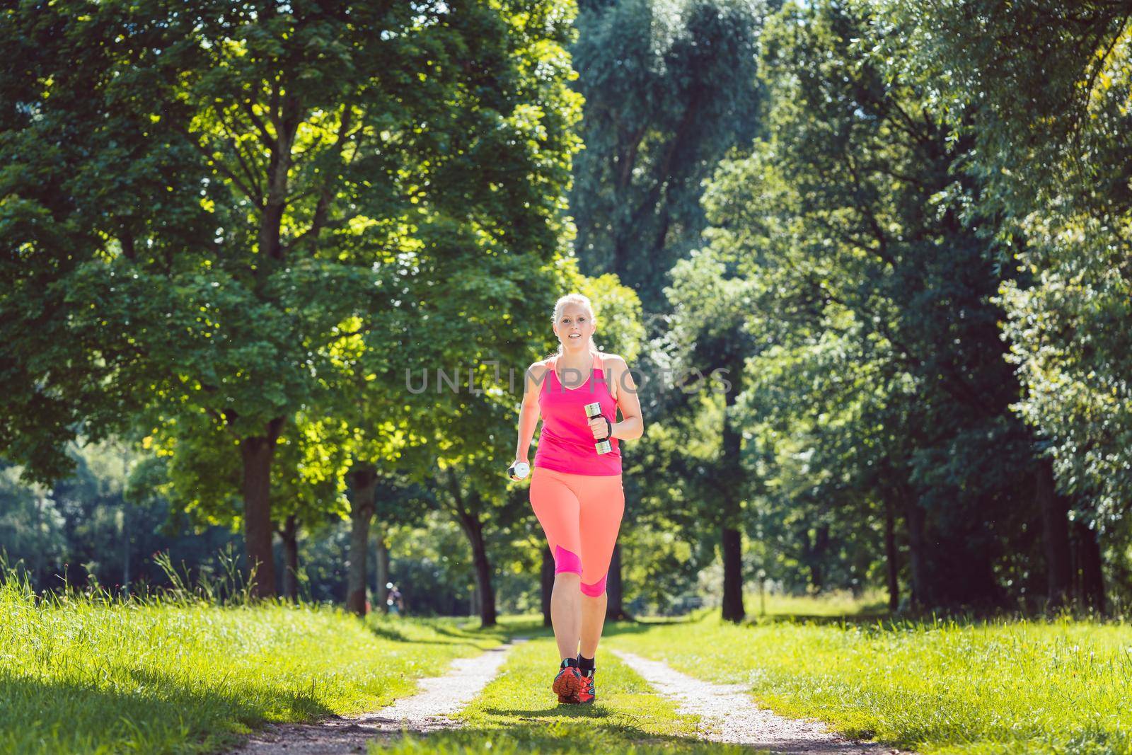 Woman running down a path on grass meadow with weight dumbbells