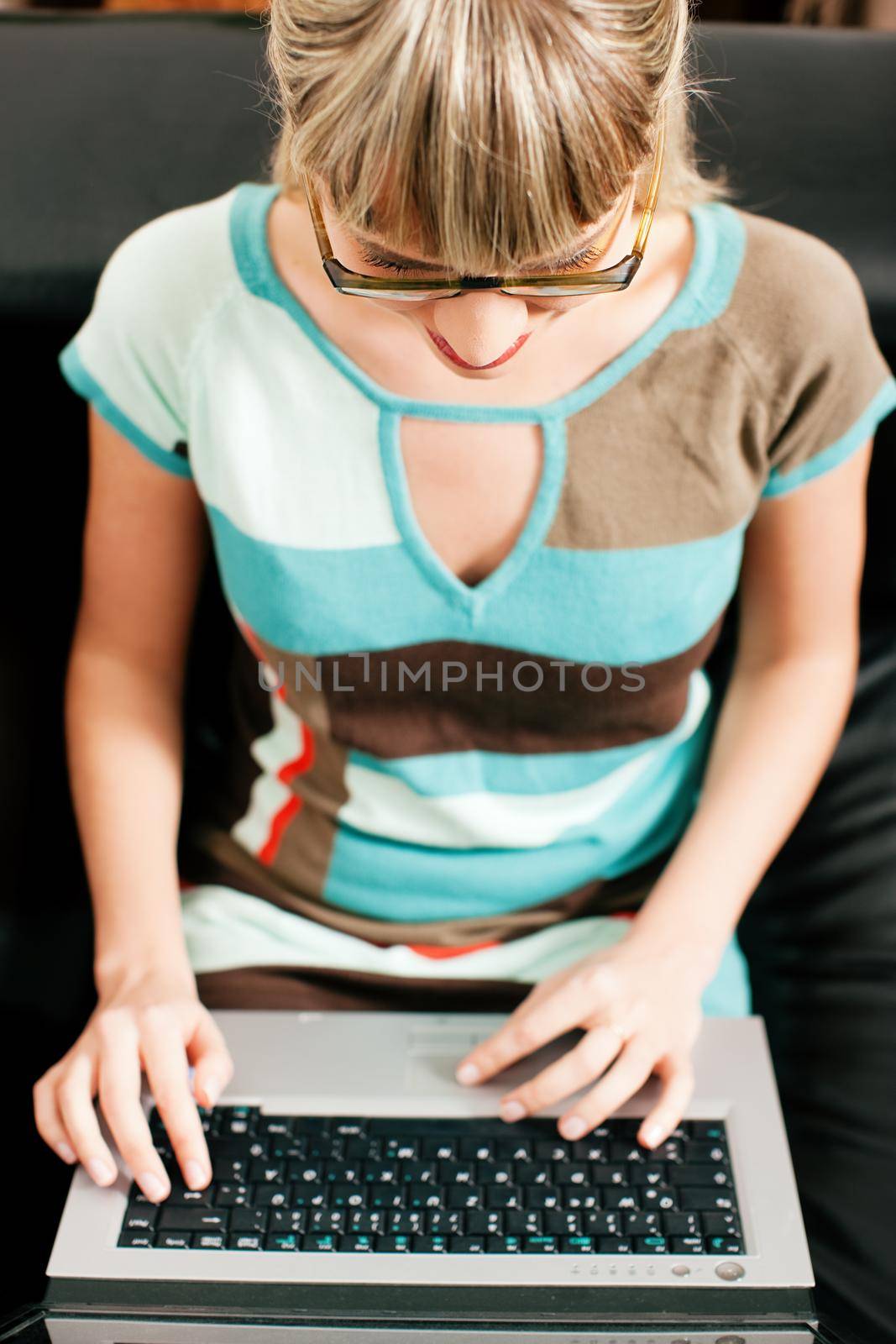 Woman - a telecommuter - doing administration of her business from a laptop sitting on a sofa in her living room