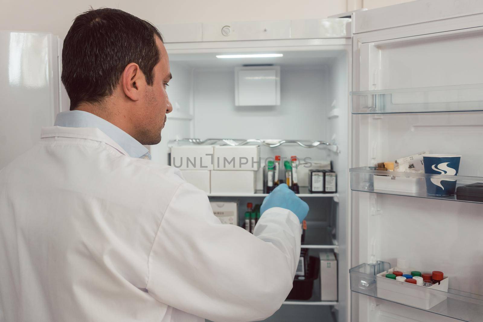 Lab technician storing blood samples in fridge by Kzenon