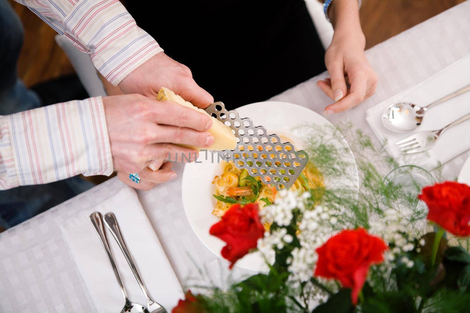 Man grating cheese over pasta, domestic setting (selective focus on the cheese grater)