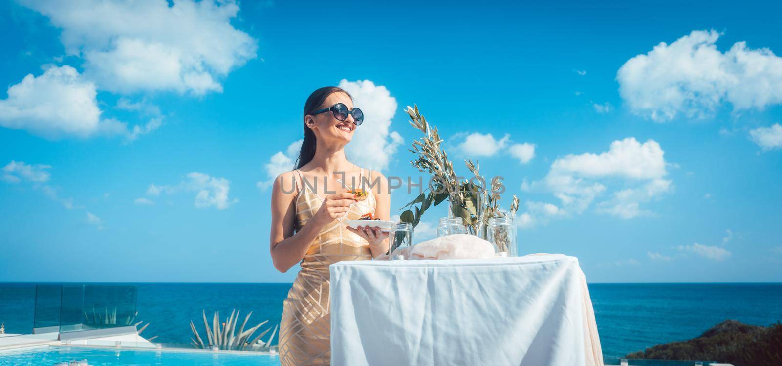 Woman in golden dress having food at beach party with pool and beach in the background