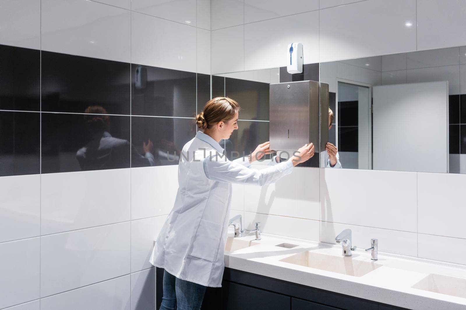 Cleaning woman refilling paper towels in public toilet or restroom