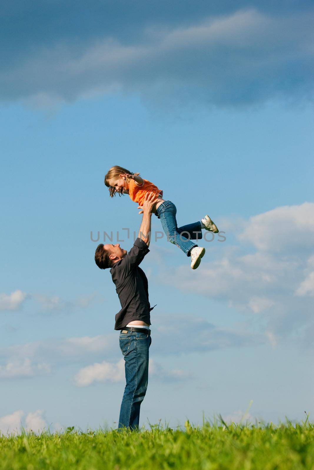 Father and his kid - daughter - playing together at a meadow, he is throwing her into the air at a late summer afternoon, family concept