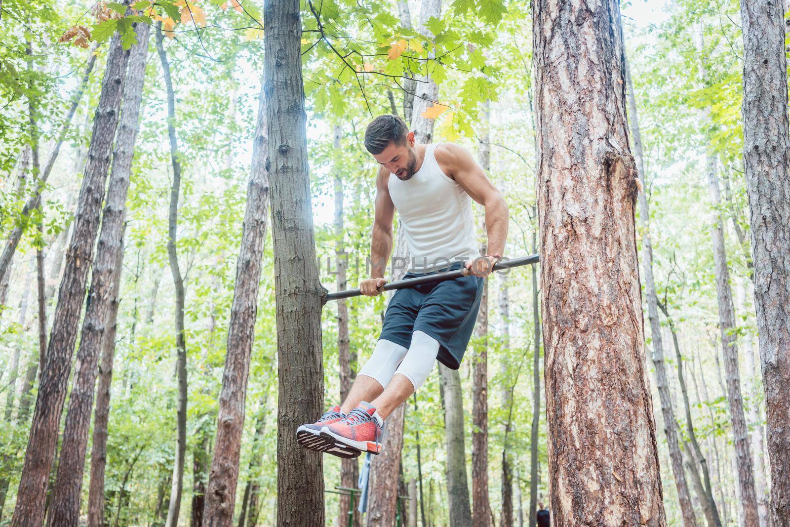 Muscular Man doing gymnastics on high bar in the woods