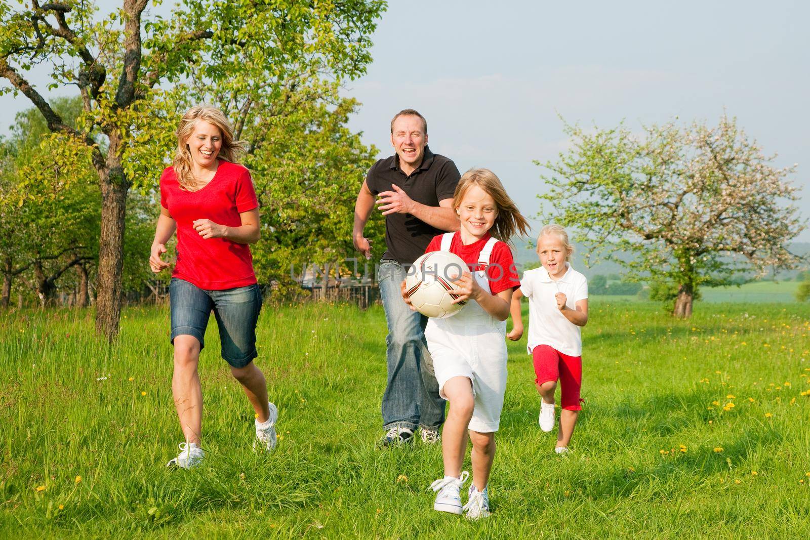 Happy family playing football, one child has grabbed the ball and is being chased by the others