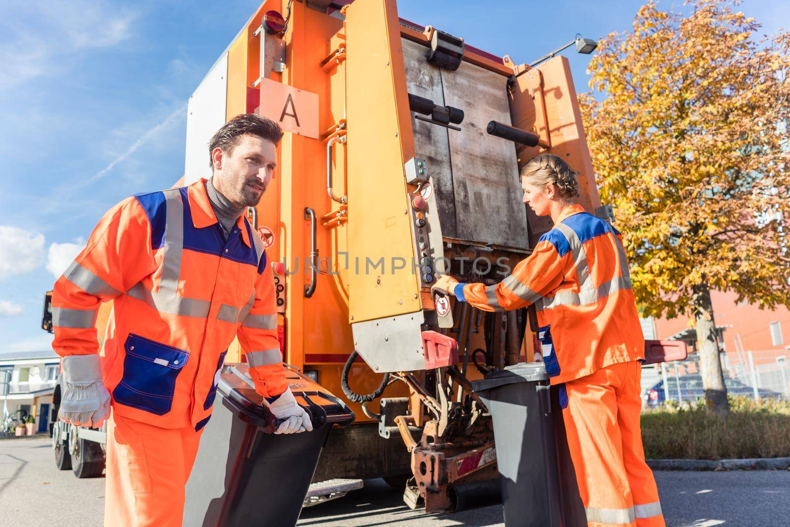 Waste collector gripping handle of garbage truck riding on the platform