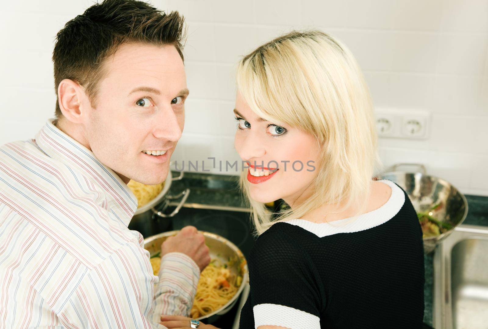 Young couple cooking in their kitchen at home, both looking into the camera