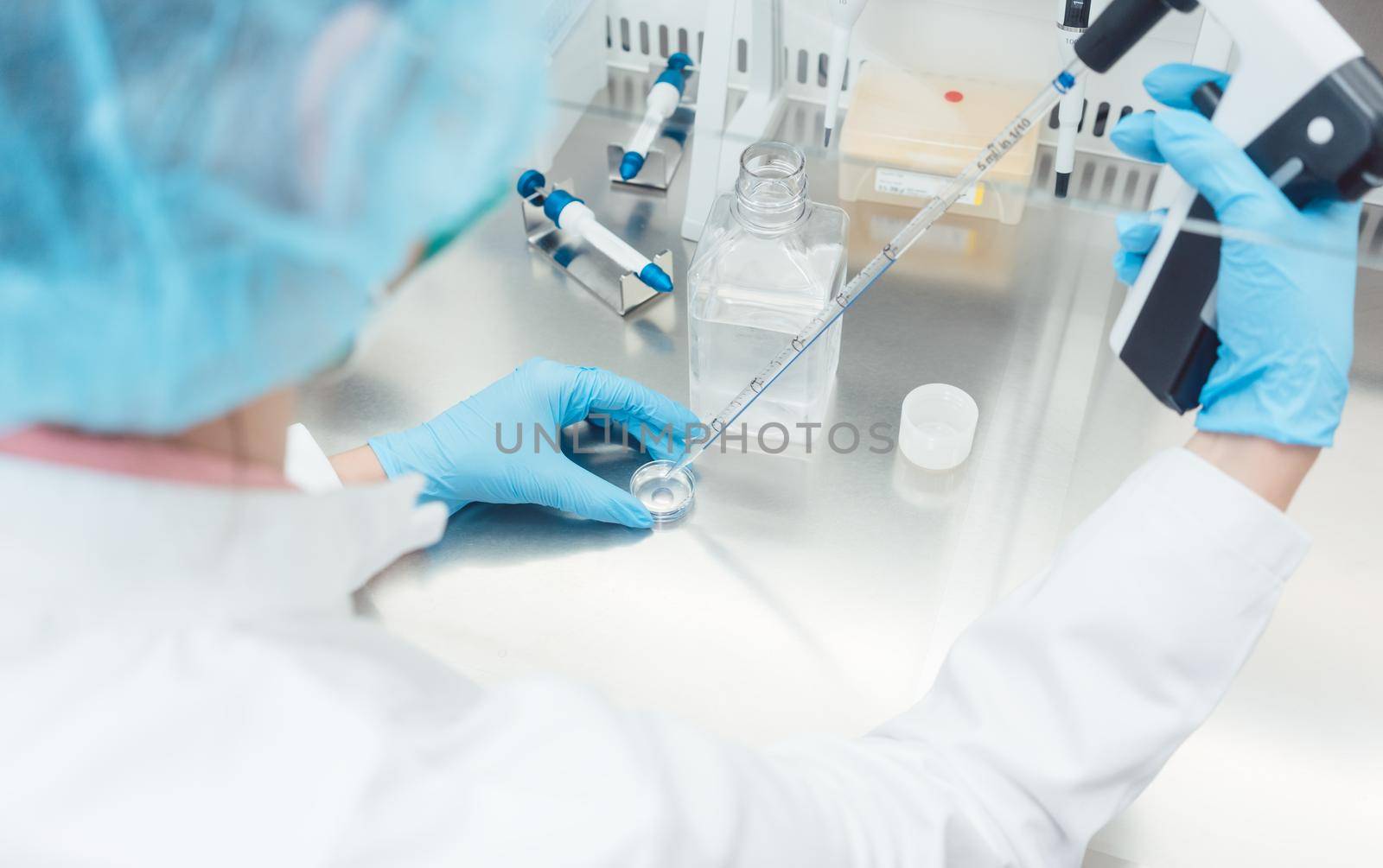 Scientist in lab conducting biotechnological experiment using pipette and petri dish