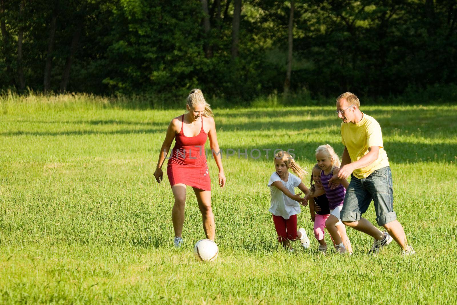 Happy family playing football (well, soccer for North America) on a green, sunlit meadow