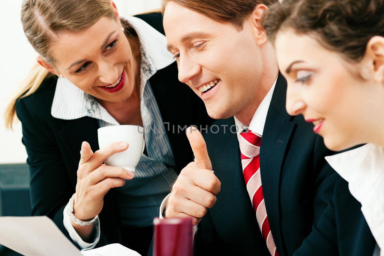 Small business team - man and two women - working in the office having a success, one woman drinking a mug of coffee