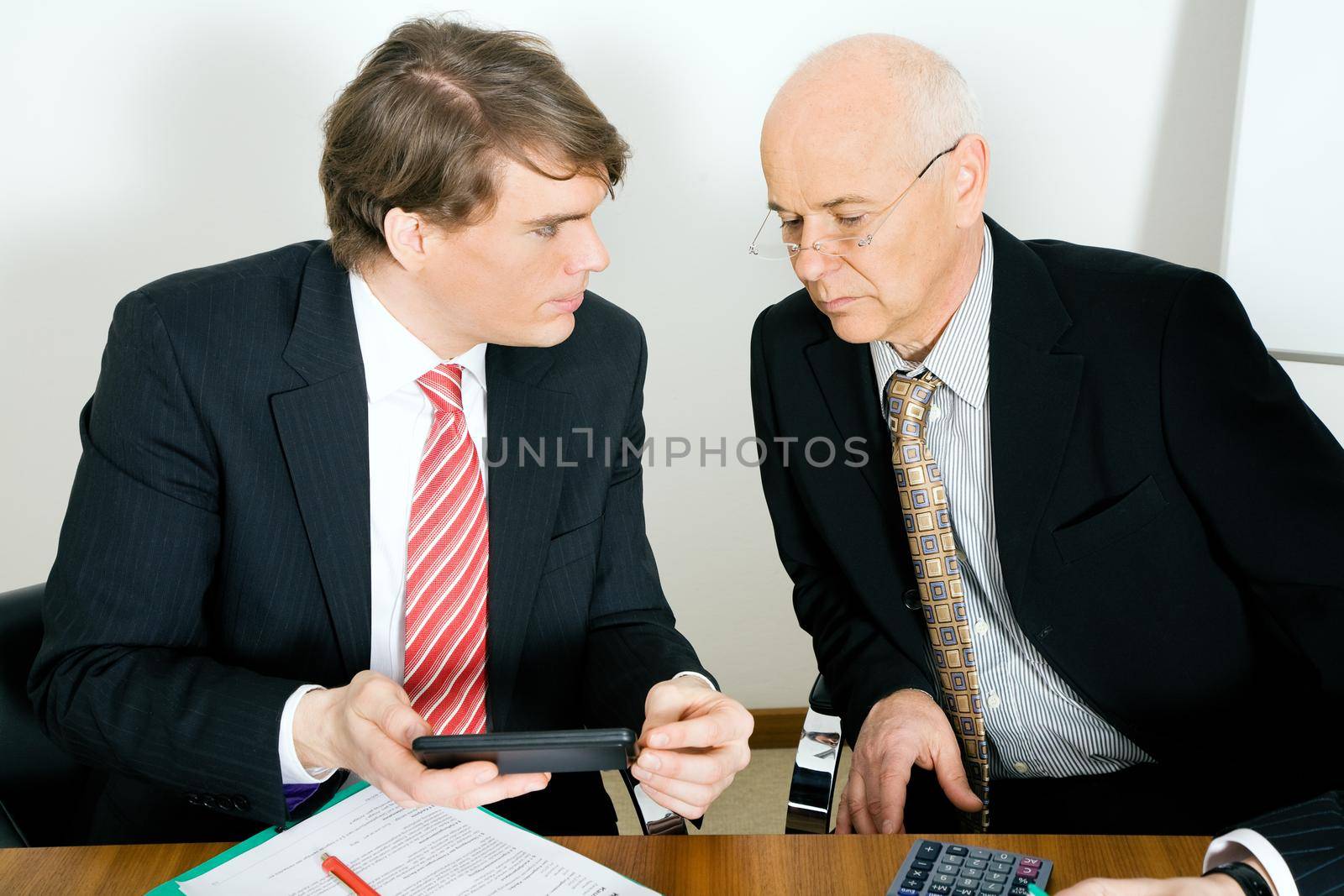 Two businesspeople crunching the numbers, the senior guy looking sceptical