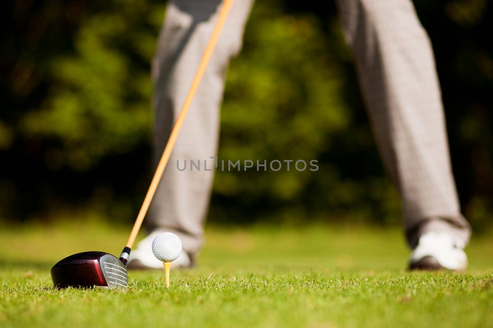 Golf player attempting the tee stroke in the teeing area (only legs of player to be seen, focus on ball)