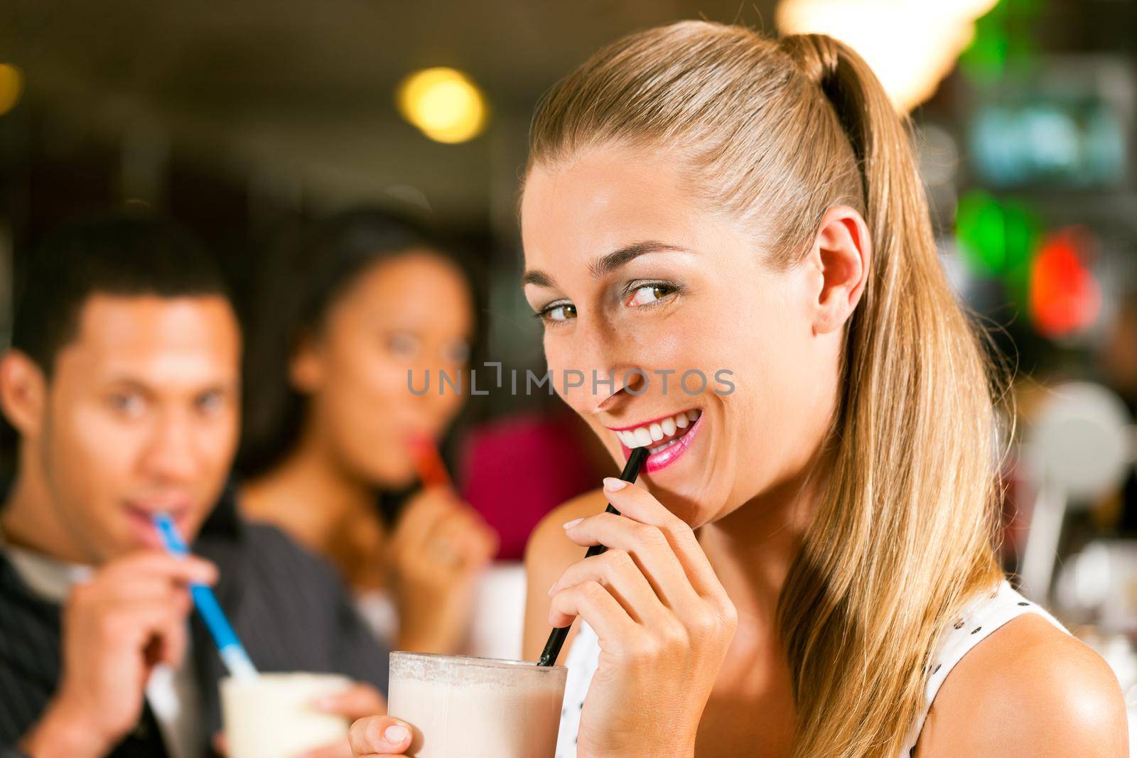 Friends drinking milkshakes in a bar and have lots of fun; focus on the woman in front