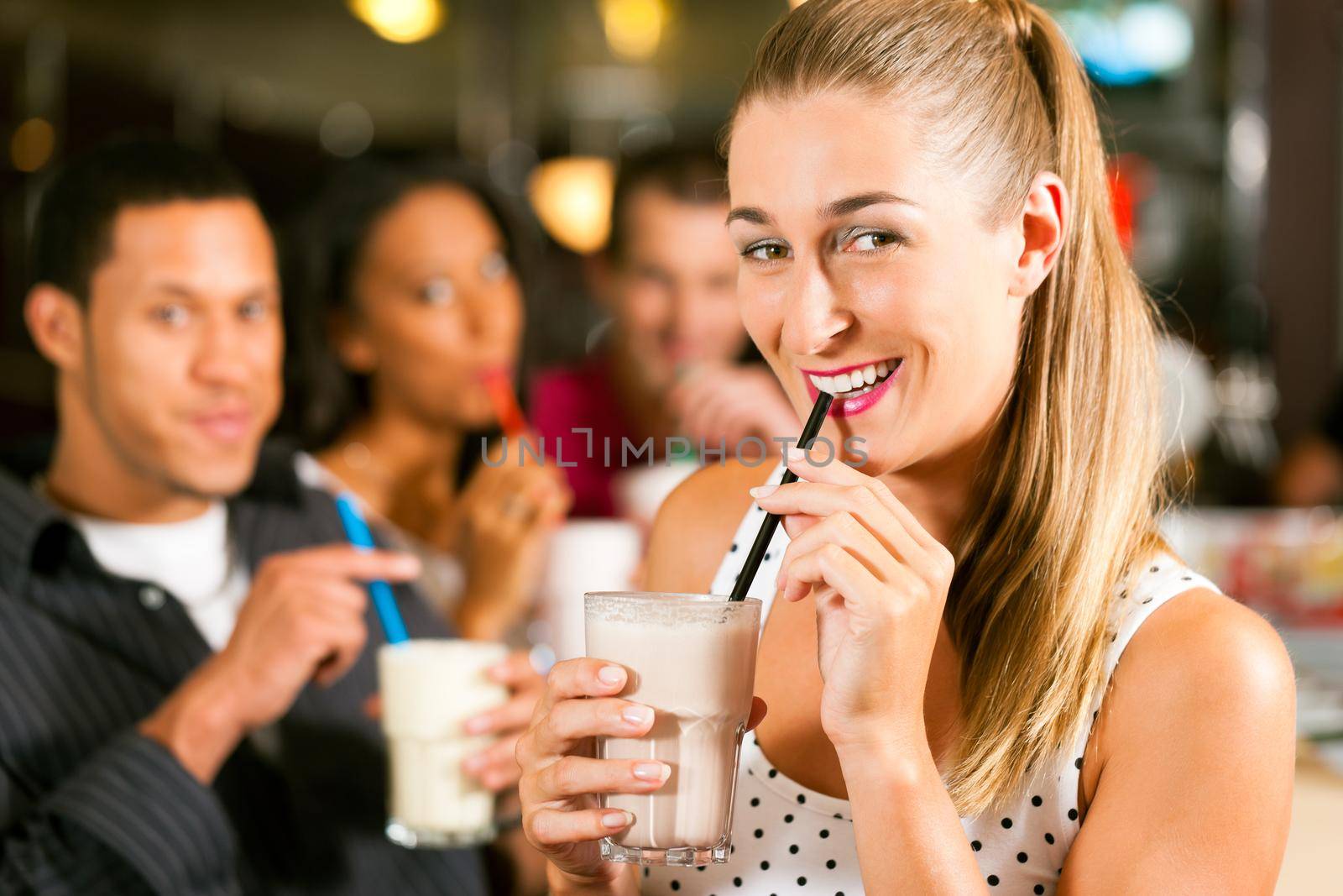 Friends drinking milkshakes in a bar and have lots of fun; focus on the woman in front