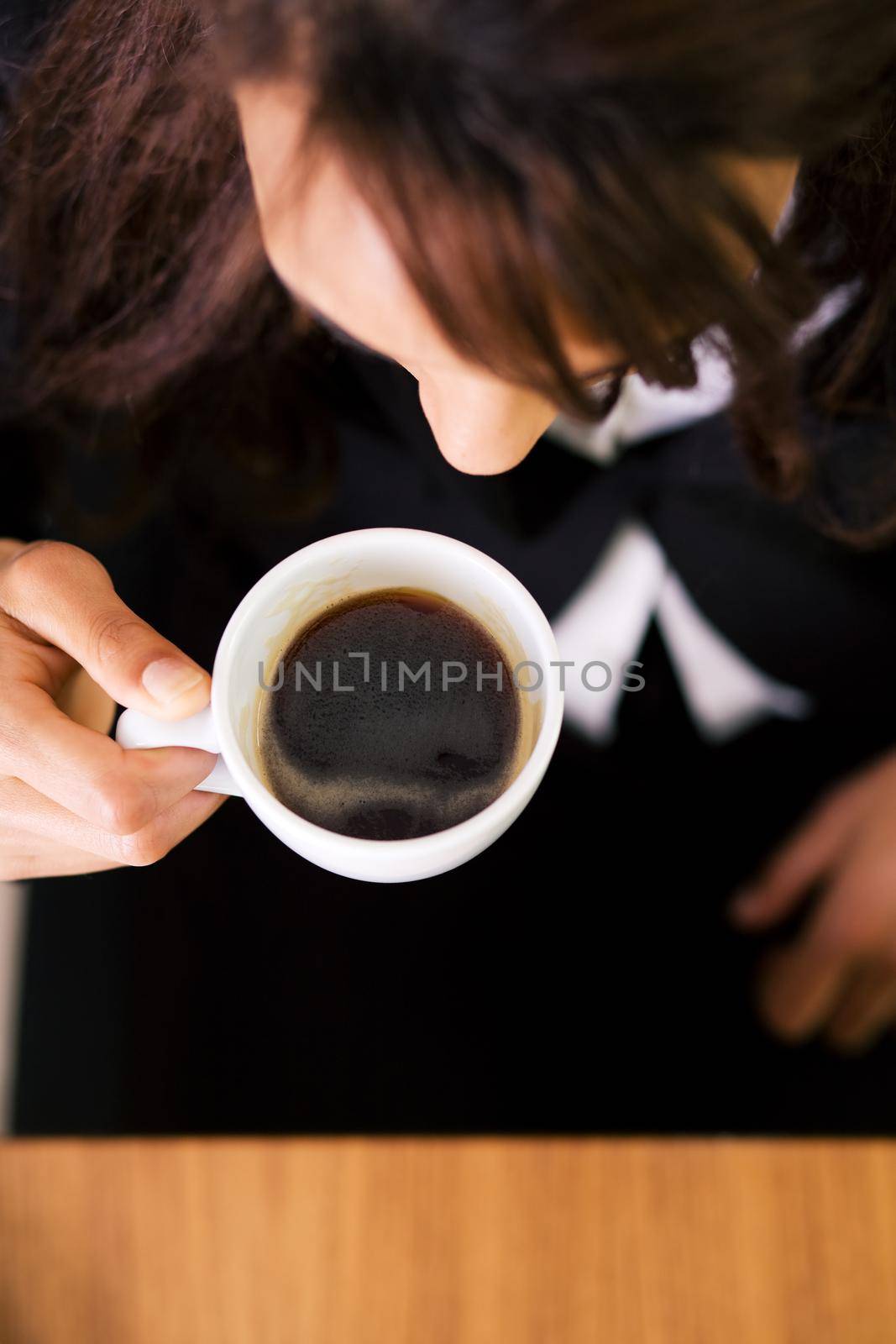 Woman pictured from above sitting on a desk having a double espresso (shallow depth of field, focus on coffee)