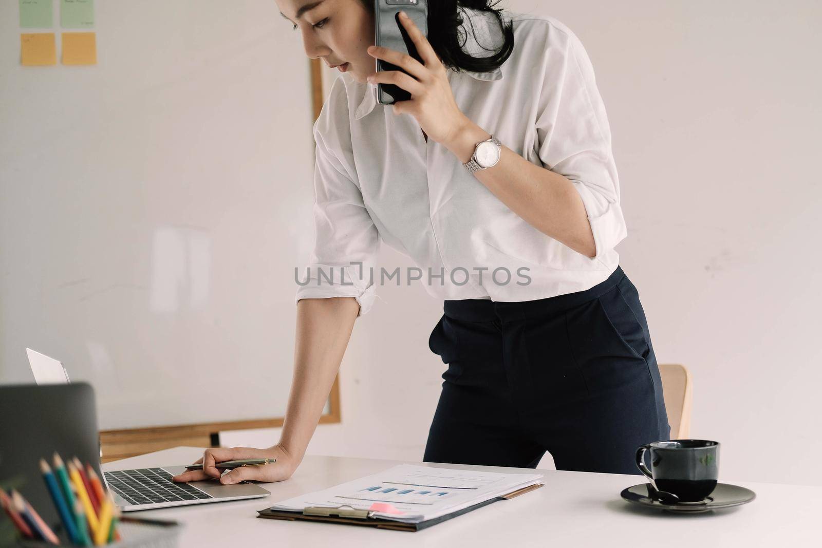 Young female entrepreneur working laptop computer and talking mobile phone to client.