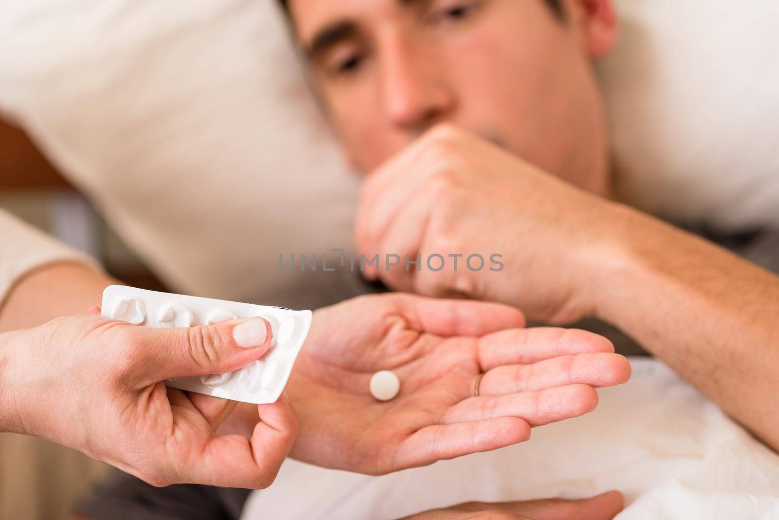 Sick man taking medication offered by a nurse who is holding a single pill in one hand and blister pack in the other