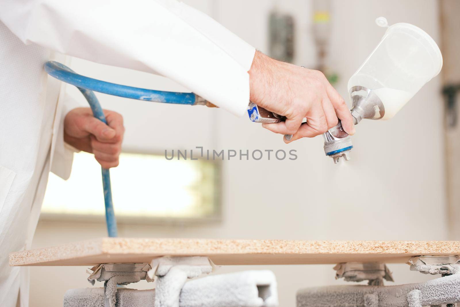 Carpenter in his paint room spraying a piece of wood to be used in his workshop later