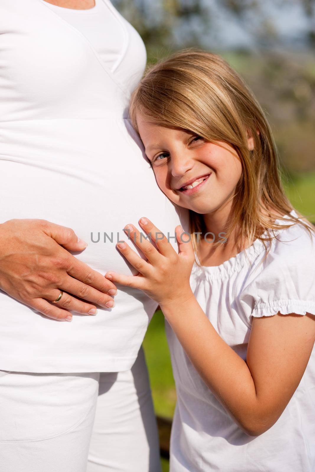 Family affairs - Girl is touching round belly of her pregnant mother in eager anticipation of the new child