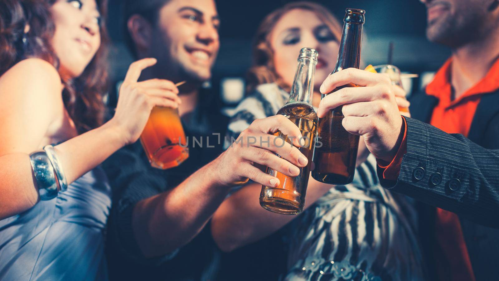 Group of party people men and women, with cocktails and beer bottles in a bar or club having fun