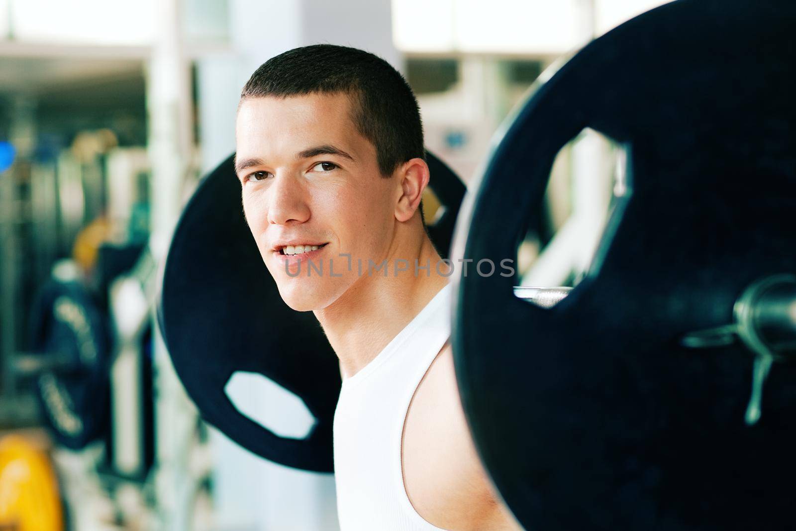 Strong and handsome man lifting weights - a barbell - in a gym