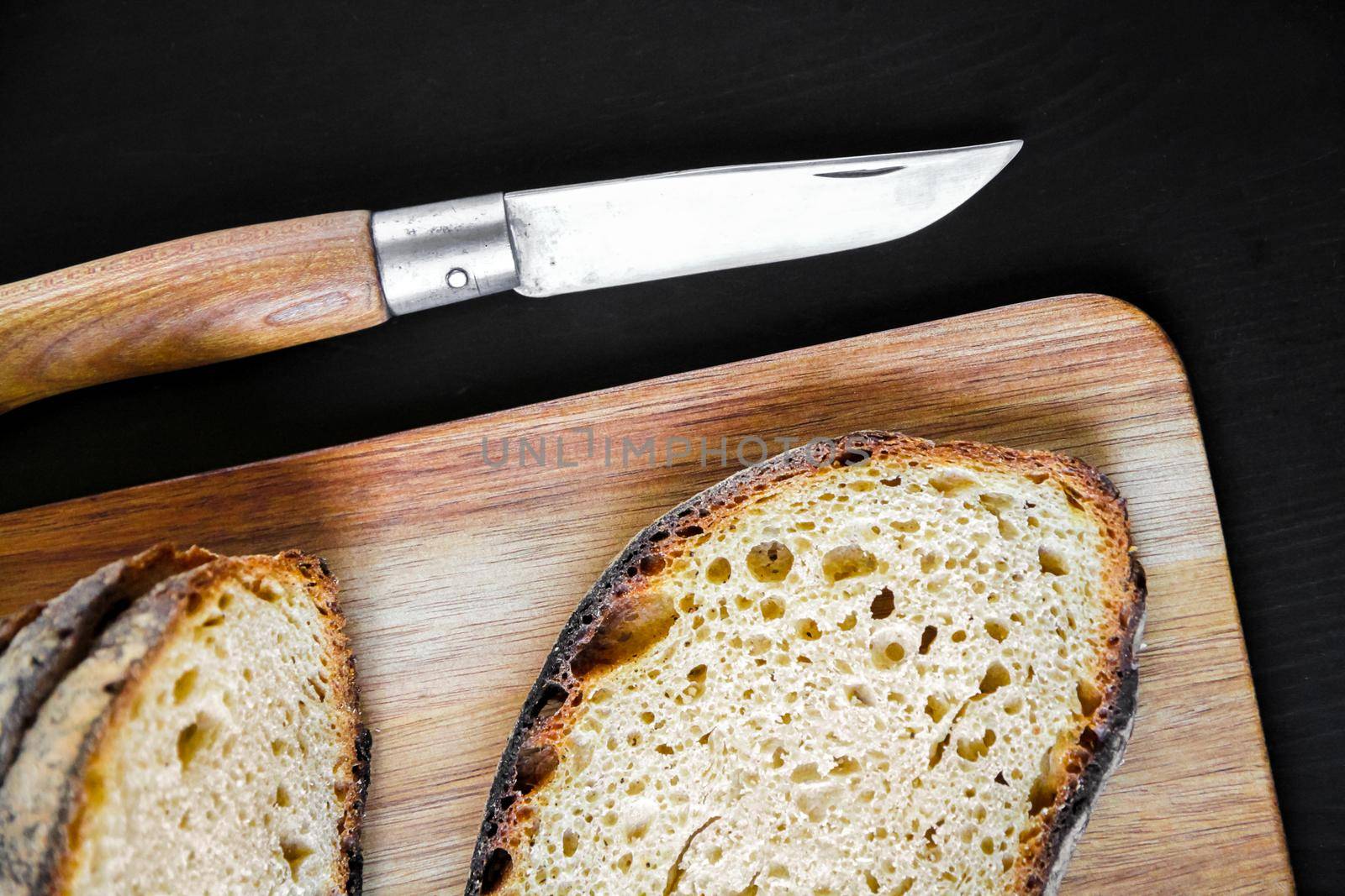 Traditional French country bread slices and pocket knife on a wooden cutting board. Top view