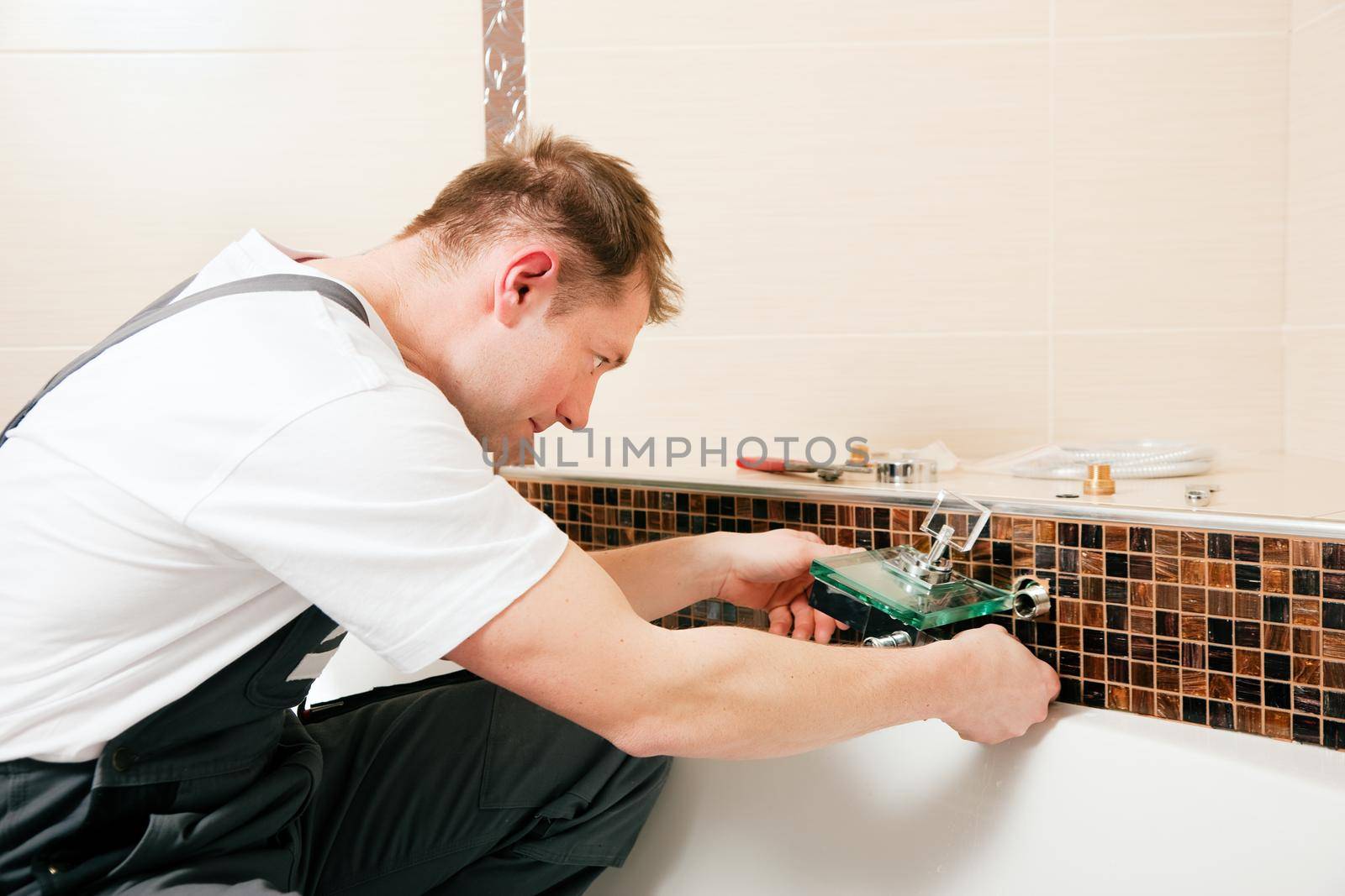 Plumber installing a mixer tap in a bathroom, he is sitting in the bathtub, focus on eyes of the man!