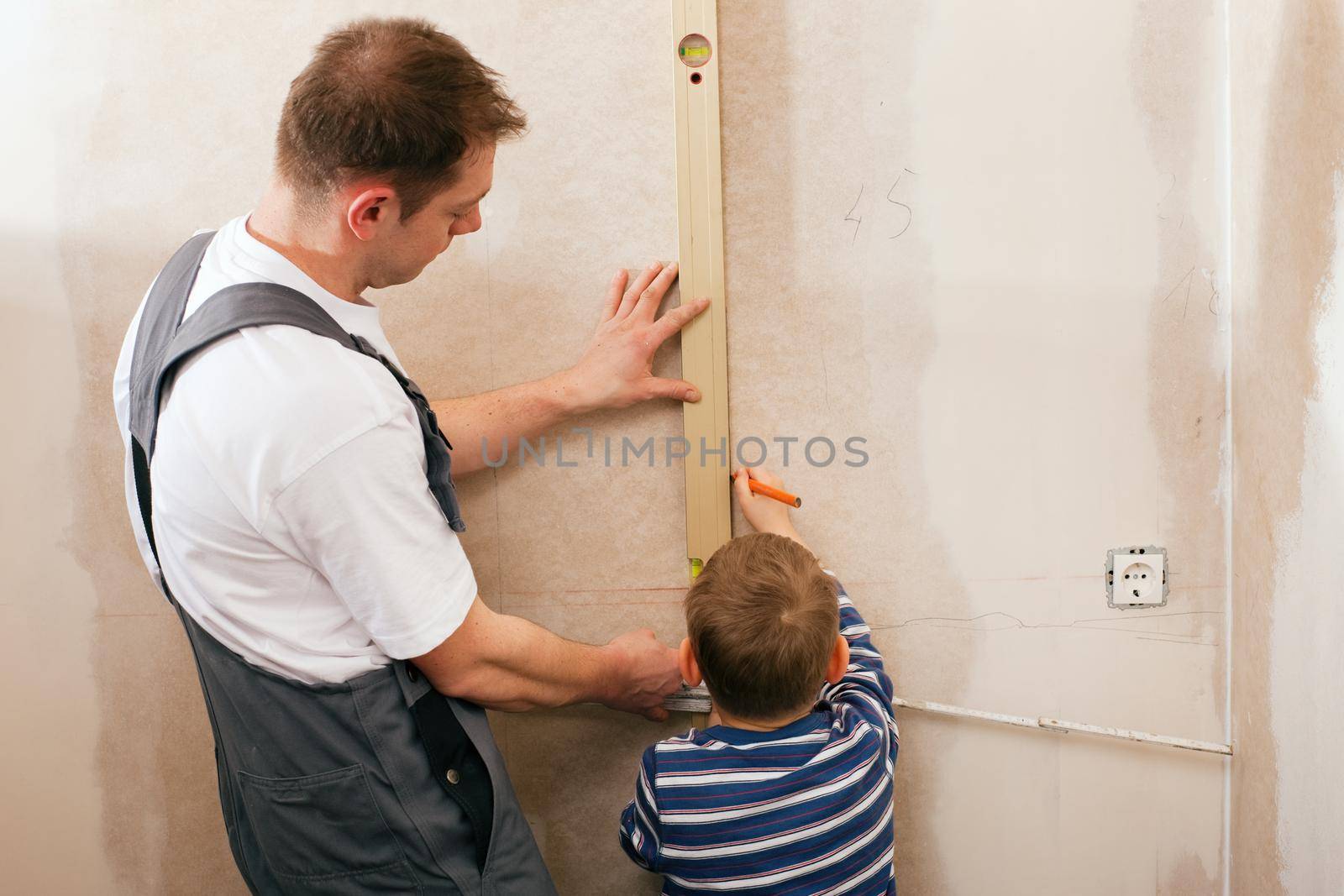 Father and son measuring a dry wall in their home with a folding rule and a bubble level