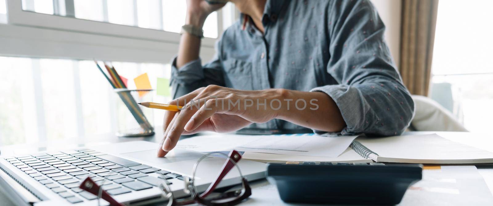 Young accountant hand holding smartphone to call marketing consultants and using laptop computer to analyze sales growth in the global workplace market. accounting concept.