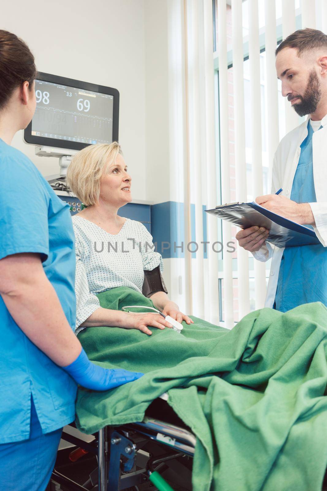 Doctor and nurse talking to patient in recovery room of hospital by Kzenon