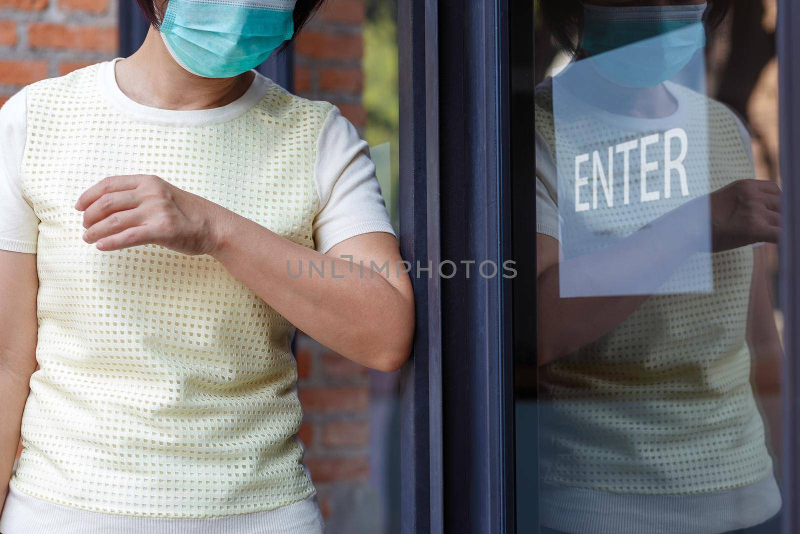 Woman wearing mask opening the door with the elbow for protection  infection COVID-19