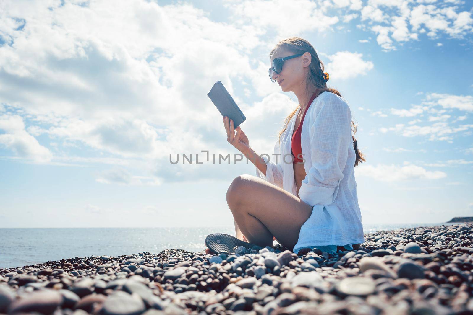Woman reading a novel on ebook by the sea in her vacation 