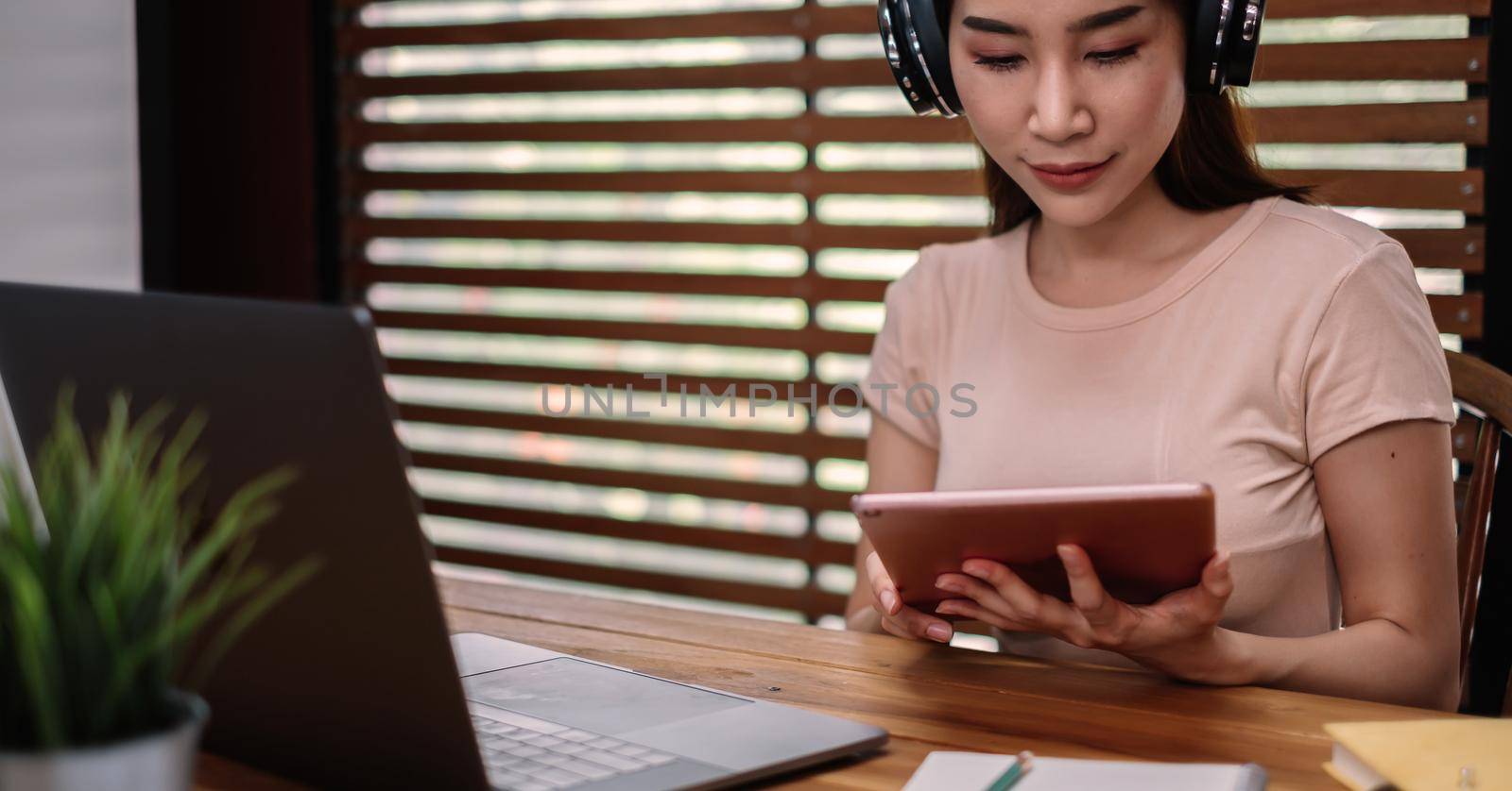 A asian female student sitting at the table, using tablet when studying online at home by nateemee