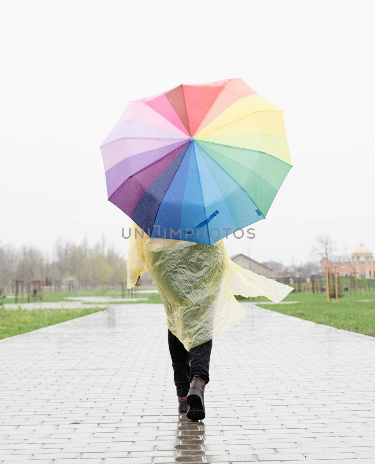 woman holding colorful umbrella walking in the rain, view from behind by Desperada