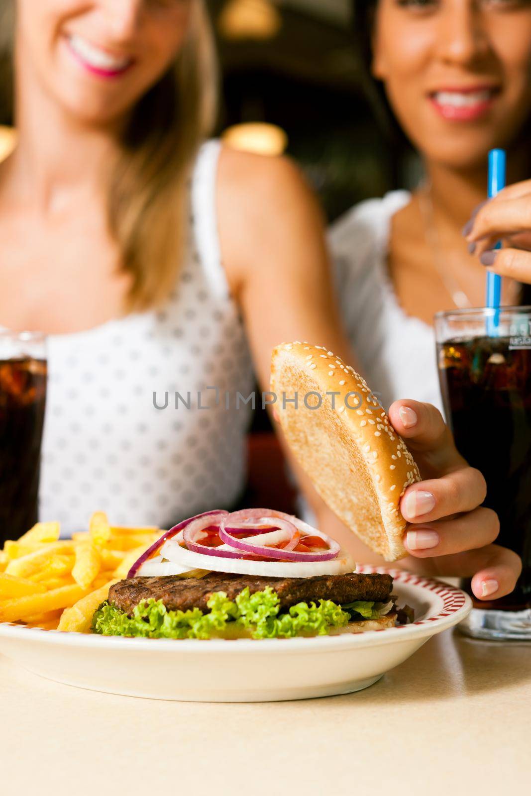 Two women eating hamburger and drinking soda by Kzenon