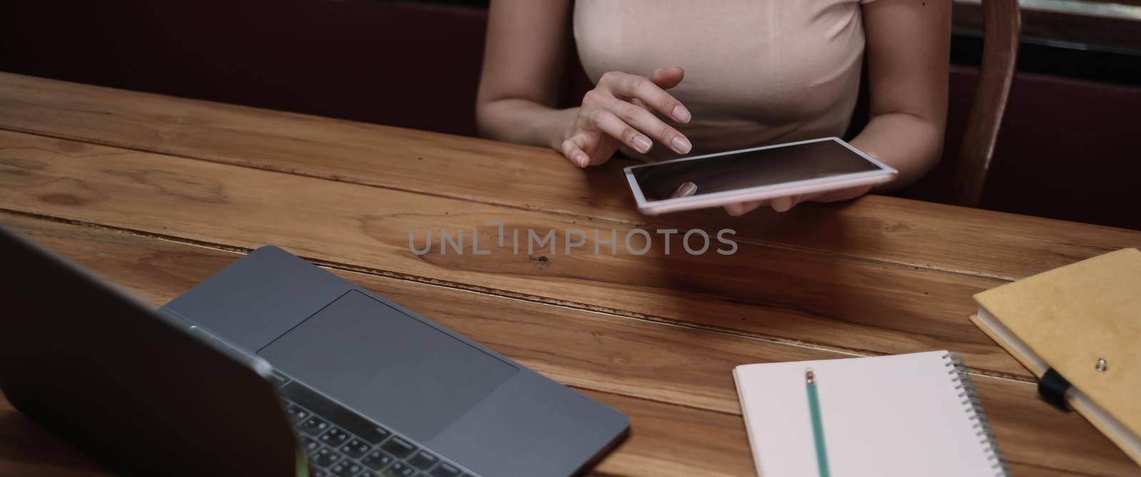 Closeup of female hands using modern digital tablet on wooden desk, young woman working or learning online at home via tablet and laptop computer