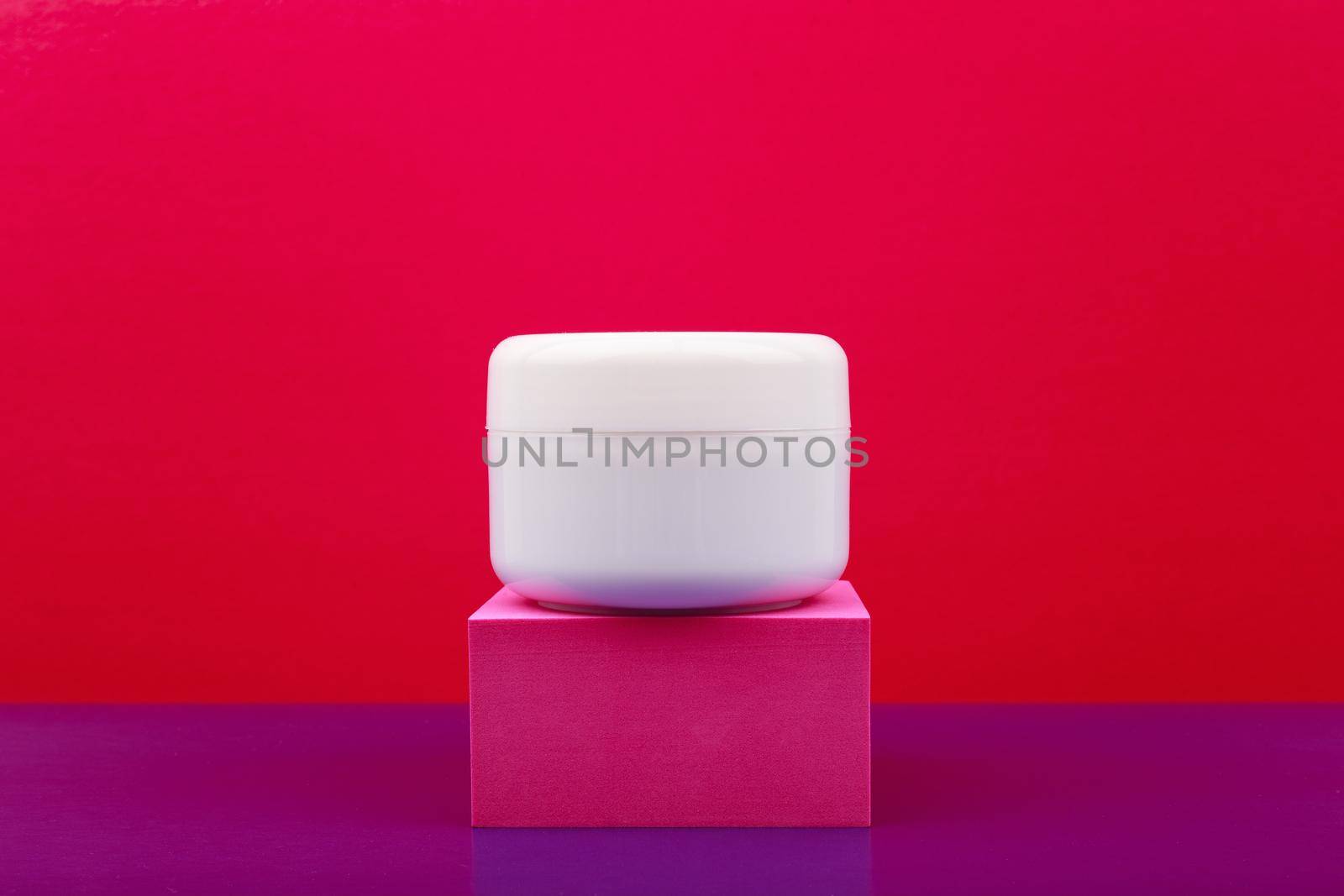 White glossy cosmetic jar on pink pedestal against red and purple background with copy space by Senorina_Irina