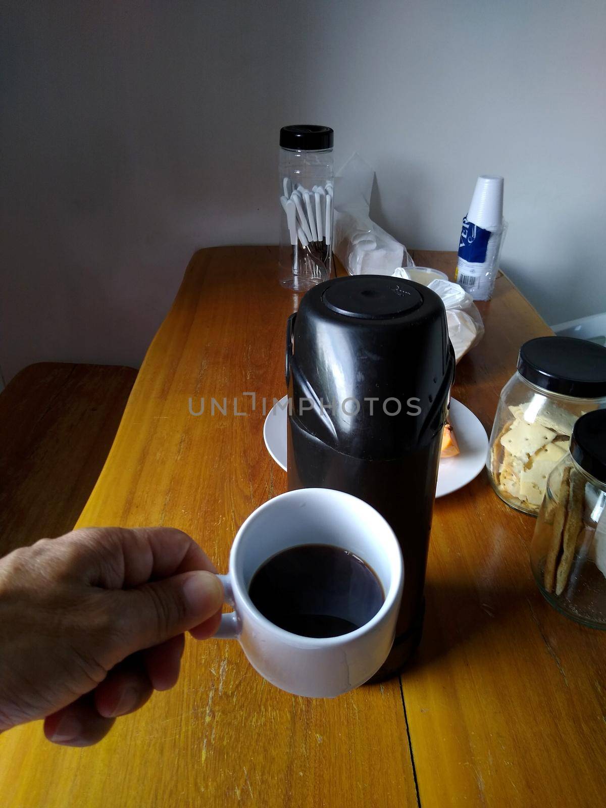 salvador, bahia / brazil - october 25, 2020: hand holds a cup of coffee next to a thermos on a breakfast table in the city of Salvador.
