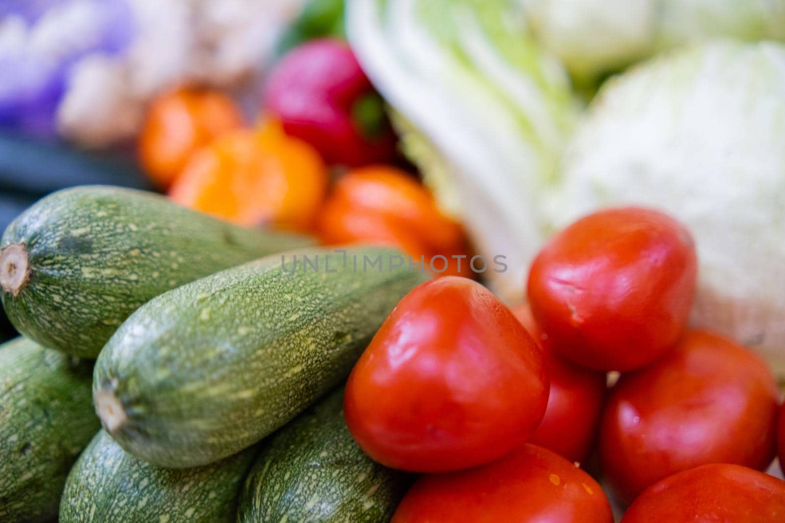 Close-up of colorful vegetable stand with tomatoes, zucchini, bell peppers and lettuce. Fresh-looking vegetables for sale on stall inside classic Mexican market. Natural healthy food