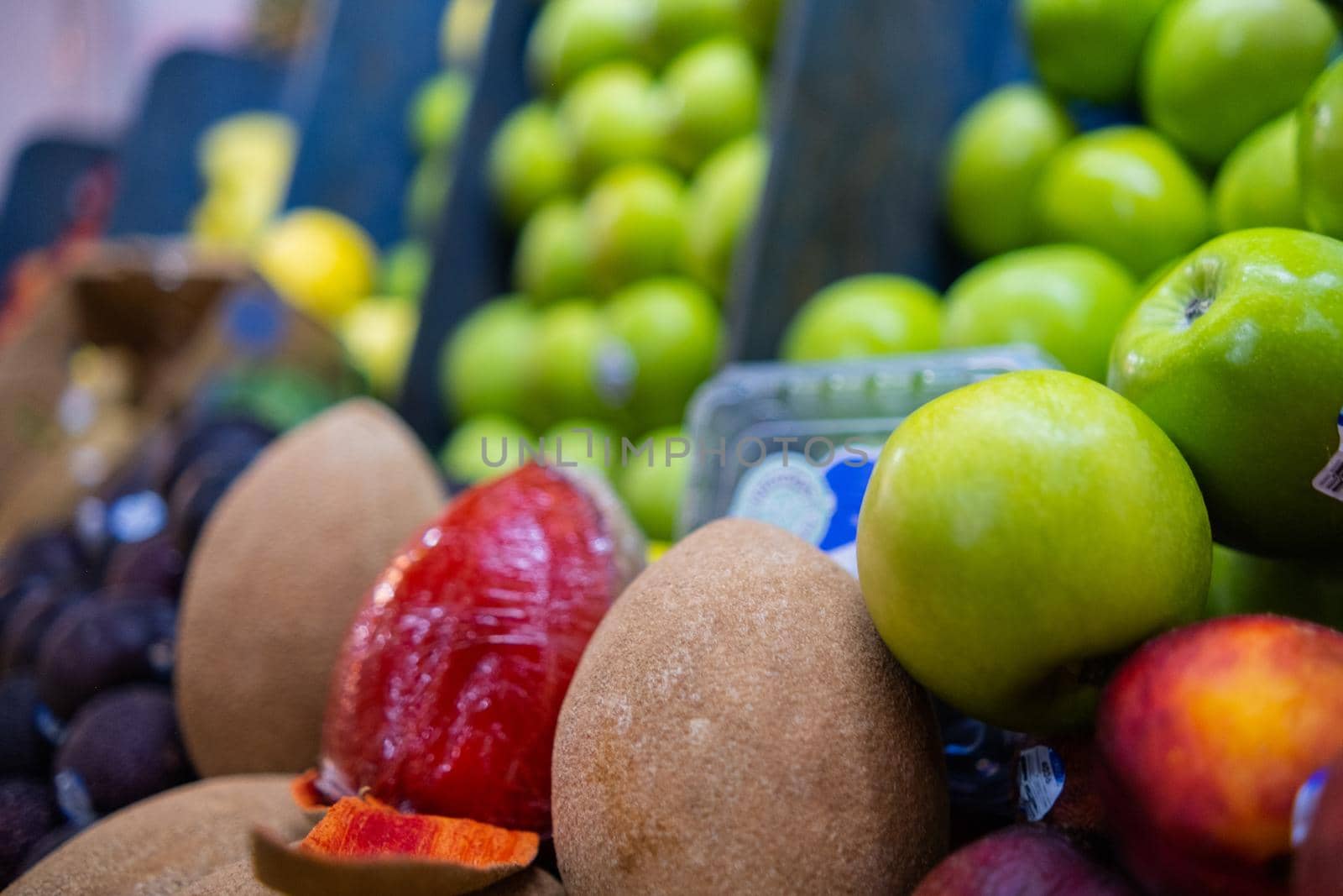 Close-up of colorful fruit stand with mamey and blurry piles of green apples as background. Close-up of juicy fruit for sale on stall inside classic Mexican market. Healthy food