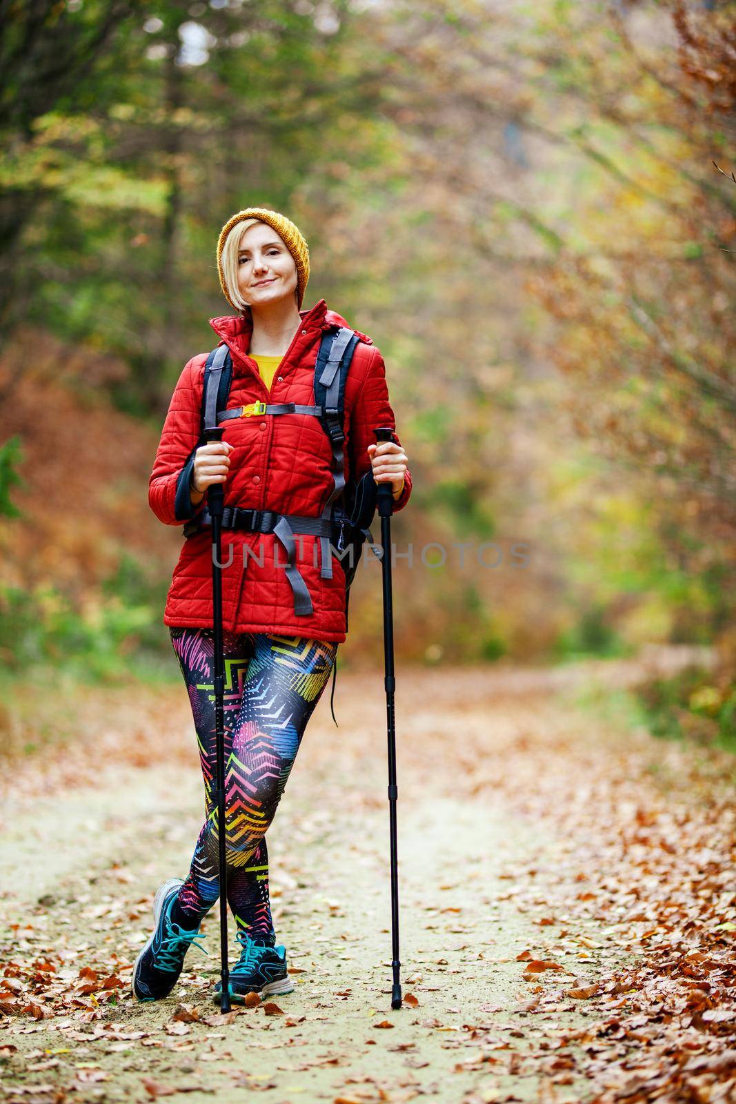 Hiking girl with poles and backpack standing on a trail. Looking at camera. Travel and healthy lifestyle outdoors in fall season
