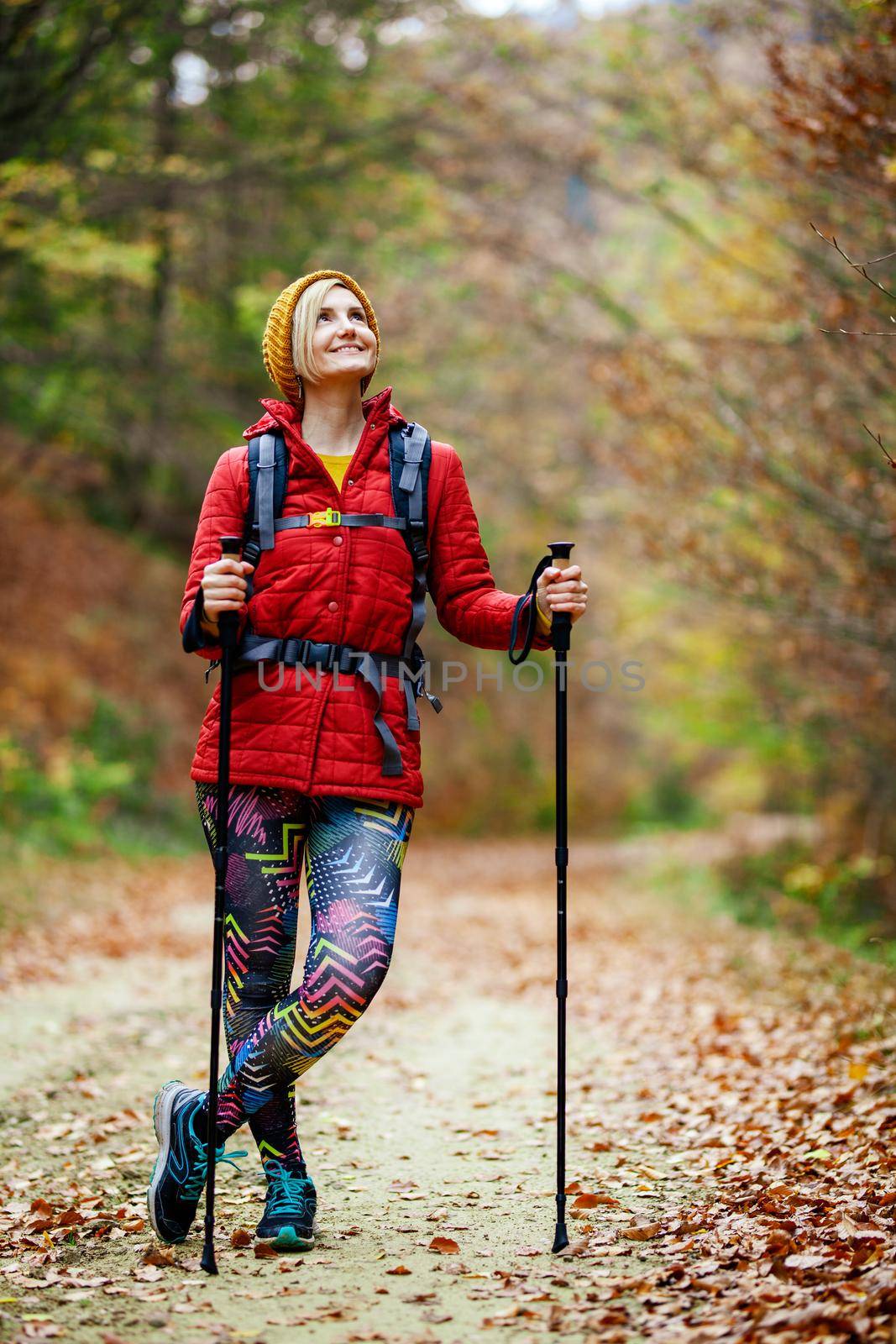 Hiking girl with poles and backpack on a trail. Looking at camera. Travel and healthy lifestyle outdoors in fall season by kokimk