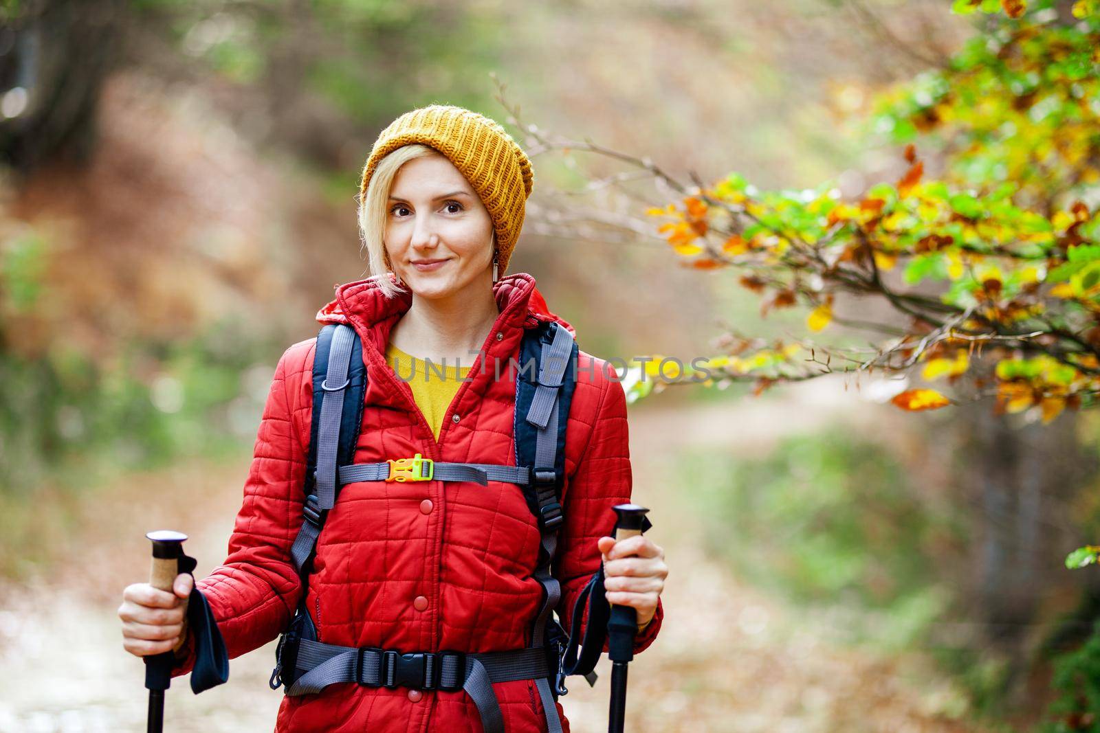 Hiking girl with poles and backpack on a trail. Looking at camera. Travel and healthy lifestyle outdoors in fall season by kokimk