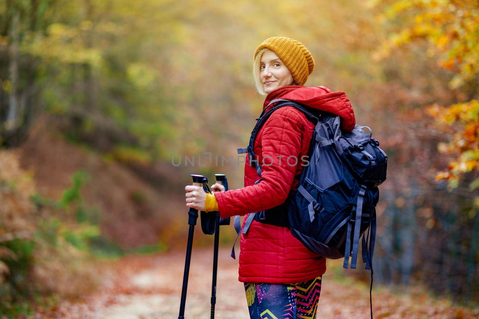 Hiking girl with poles and backpack standing on a trail. Looking at camera. Travel and healthy lifestyle outdoors in fall season